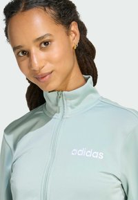 Mint green zip-up jacket made of soft fabric; features a high collar and white embroidered "adidas" logo on the left chest area.
