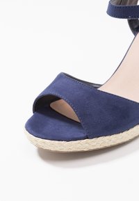 Námořnické modré semišové klínové sandály s otevřenou špičkou, s tkanou juteovou podrážkou a nártním páskem, které vynikají hladkou texturou a čistými liniemi.