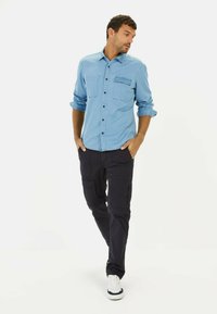 Lichtblauwe denimshirt met twee borstzakken en zwarte knopen; gecombineerd met marineblauwe cargobroek met zijzakken en een lichte glans.