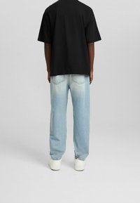 Camiseta de algodón negra de manga corta, combinada con jeans de mezclilla azul claro con un lavado descolorido y costuras visibles. Zapatillas blancas.