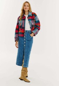 Mnohofarebný károvaný kabát s modrými, červenými a oranžovými pruhmi, džínová sukňa s prednými gombíkmi a béžové čižmy po kolená.