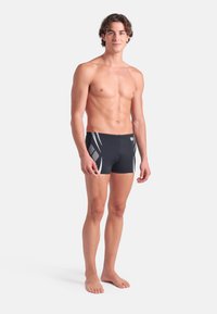 Svarta simshorts med vita snedstreck, tillverkade av stretchy material, åtsittande design, midja till låret längd. Slät textur, inga synliga detaljer.
