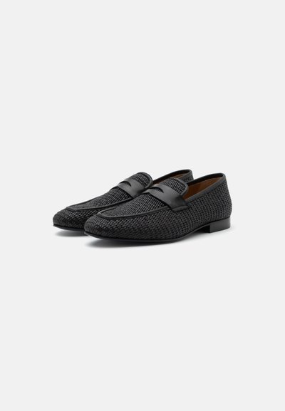 Μαύρα υφαντά δερμάτινα loafers με λεπτομέρεια λουριού penny και χαμηλό τακούνι, τοποθετημένα δίπλα δίπλα σε λευκό φόντο.