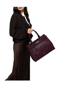 Woman in dark brown outfit holding a large textured burgundy handbag with top handles and silver clasp detailing.