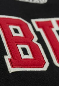 Tessuto nero con lettere ricamate in rilievo rosse e bianche, caratterizzato da dettagli in un carattere audace e un motivo geometrico attorno alle lettere.