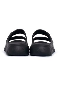 Sandales noires à enfiler, avec un dos ouvert, comportant trois lanières horizontales et une semelle textured. Le logo "Buffalo" est embossé sur le talon.