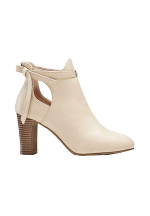 Bottine beige avec une finition en cuir lisse, bout pointu, découpe sur le côté et un détail noué à l'arrière ; dotée d'un talon en bois empilé.