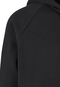 Közeli kép egy fekete kapucnis pulóver vállvarrásáról és a kapucni egy részéről, sima anyagtextúrával.