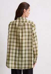 Long-sleeve plaid shirt in light yellow with dark green and brown checks, featuring a button-down collar and a relaxed fit design.