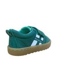 Zapato para niño pequeño de cuero verde con una suela de goma marrón. Presenta detalles en blanco y tiras de Velcro para facilitar el uso. Material suave y texturizado.
