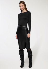 Czarna dopasowana bluzka z długim rękawem zestawiona z midi spódnicą z wysokim stanem z skórzanym przodem z rozcięciem. Założona z wysokimi, teksturowanymi czarnymi kozakiem do kolan.
