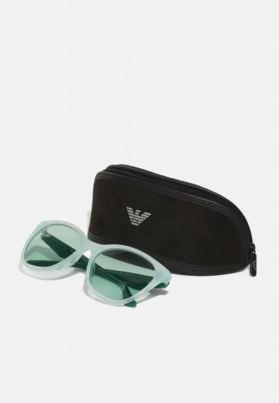 Mint green oversized sunglasses with dark green lenses, accompanied by a black zipped case featuring a logo. Soft texture on the case.