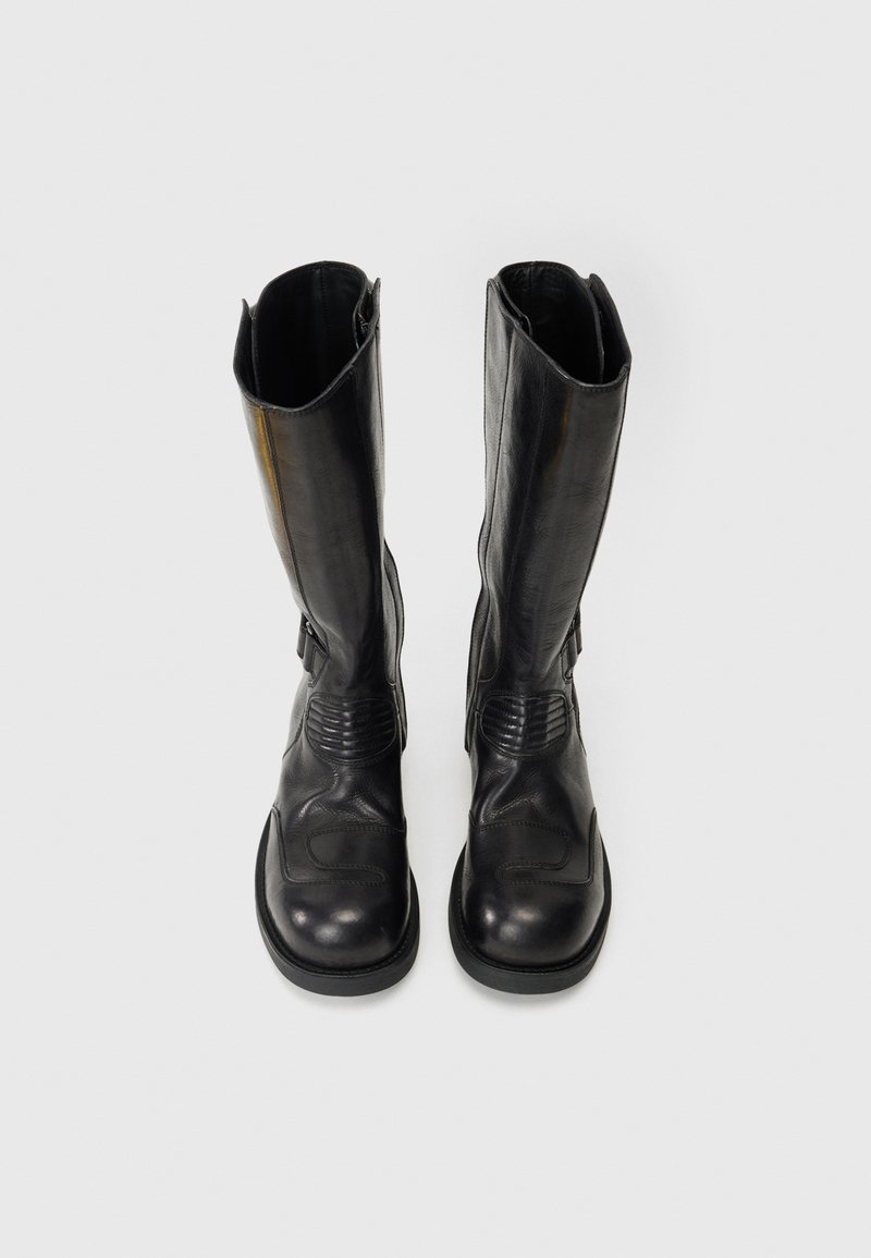 Bottes en cuir noir montantes jusqu'au genou avec un bout arrondi, des accents texturés sur les côtés et une semelle en caoutchouc robuste. Possède une finition lisse et un design minimaliste.