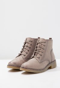 Taupe kožené kotníkové boty se zaoblenou špičkou, vázáním v přední části a nízkým blokovým podpatkem. Mají texturovaný povrch a prošité detaily.
