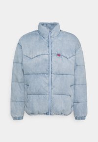 Veste matelassée bleu clair avec un design en quilting, col haut, fermeture éclair avant et poignets en elastique. Comprend des poches latérales et un petit logo.