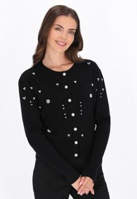 Svart ribbade kavaj med pärlknappar och blommönster. Långa ärmar och rund halsringning. Elegant, texturerad design.