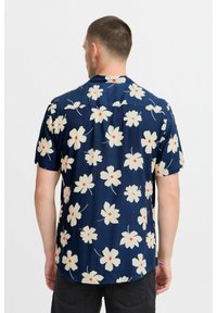 Camicia a maniche corte blu navy con motivo floreale bianco e dettagli rossi. Tessuto leggero con vestibilità comoda e orlo curvo.