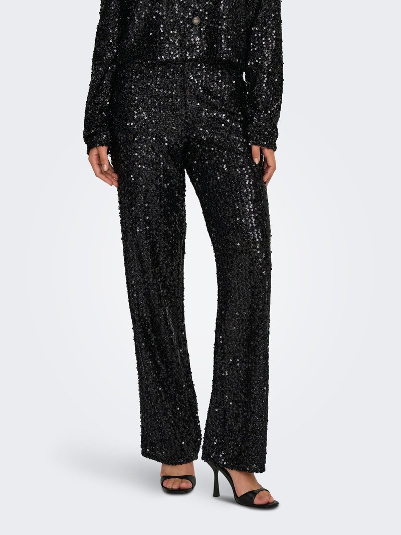 Pantaloni neri con paillettes a vita alta abbinati a top coordinato e sandali neri con tacco alto e punta aperta indossati da una persona su sfondo semplice.