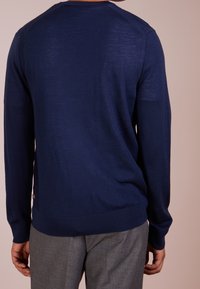 Granatowy sweter z długimi rękawami, z prążkowanymi mankietami i dołem, o prostym wzorze. Gładka tekstura i lekki materiał.