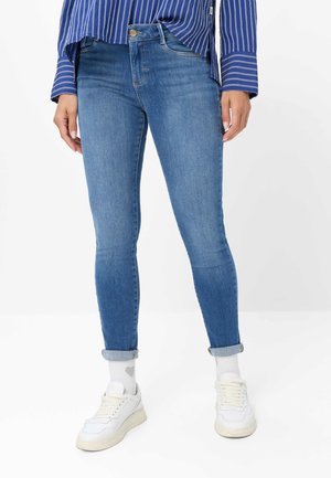 Persoon met opgerolde blauwe skinny jeans, witte sokken met hartjespatroon, witte sneakers en een blauw gestreept shirt.