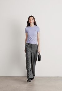 Lys lilla kortærmet t-shirt, parret med grå stribede brede bukser. Modellen bærer en lille sort håndtaske. Enkel og moderne design.