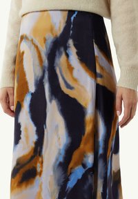 Jupe maxi en tissu doux avec un motif tie-dye orange, marine et bleu ciel. Le design présente une silhouette fluide et une texture lisse.