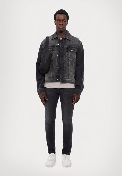 Denim jacket in dark gray with button front and two chest pockets, paired with dark jeans and white sneakers. Crossbody bag on shoulder.