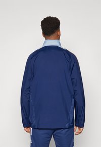 Navy windbreaker jas met lichtblauwe kraag en schouderaccenten, elastische manchetten en een gladde buitenkant.