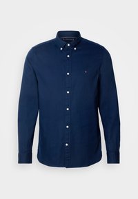 Chemise boutonnière à manches longues bleu marine en coton avec un col classique, des boutons blancs et un petit logo sur la poitrine.