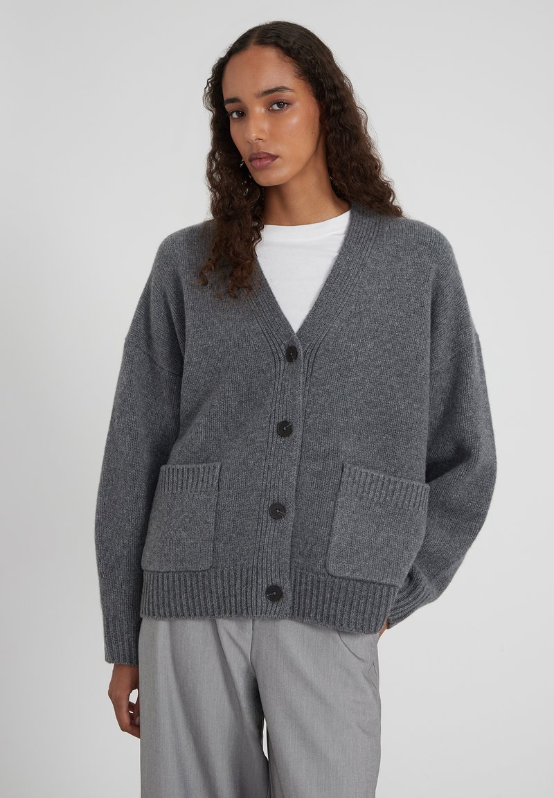 Cardigan gris en tricot avec un col en V, une fermeture boutonnée à l'avant et des poches plaquées. Caractérisé par des poignets et un ourlet côtelés, un tricot texturé et une coupe décontractée.