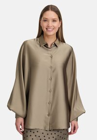 Blusa di raso verde oliva con colletto classico, chiusura a bottoni e maniche larghe, caratterizzata da una texture liscia e una vestibilità morbida.
