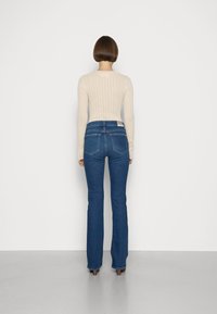 Top de manga larga de canalé color beige combinado con jeans de campana azul oscuro, con una cintura alta y dos bolsillos traseros. Diseño sencillo sobre un fondo blanco.