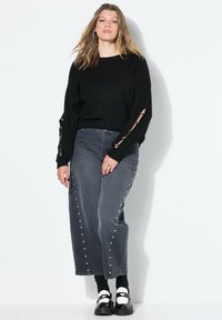 Suéter negro de punto con detalles recortados en las mangas, combinado con jeans de pierna ancha grises que cuentan con tachuelas plateadas a lo largo de las costuras laterales y zapatos de plataforma negros.
