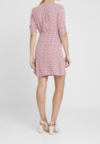 Rode bloemenjurk met een ontspannen pasvorm, korte mouwen en een cinched taille. De zoom is iets gebogen. Gecombineerd met beige blokhakken sandalen.