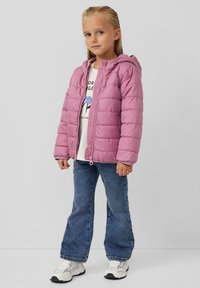 Roze pufferjack met capuchon, gewatteerd ontwerp, ritssluiting aan de voorkant, gecombineerd met een witte shirt en blauwe flare jeans. Witte sneakers maken de outfit af.