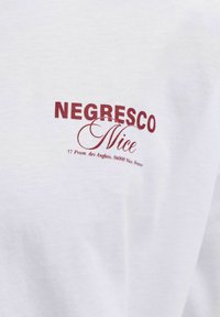 Λευκό ύφασμα με κόκκινο κείμενο που γράφει "NEGRESCO Nice" και μικρότερο κείμενο με διεύθυνση στη Νίκαια, Γαλλία, σε ένα ένδυμα.