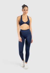Marinblå sport-bh med halterneck-design och korsad framdel, tillsammans med högmidjade leggings med ett strukturerat mönster längs sidorna.