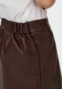 Jupe en simili cuir marron avec une taille froncée, dotée d'une poche latérale et d'une texture lisse et brillante.