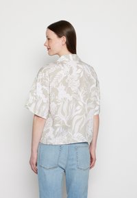 Camisa de manga curta, com colarinho, em tecido bege claro com padrão floral branco. Corte descontraído, bainha reta e textura suave.