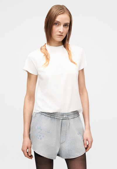 Biele tričko s krátkym rukávom a okrúhlym výstrihom, doplnené svetlomodrými rifľovými šortkami s kvetinovými ozdobami a elastickým pásom.