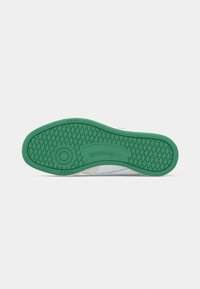 Zelená guma na bielom tenisku Reebok zobrazenom zospodu, ktorý má diamantový vzor na podrážke a okrúhly dizajn protišmyku.