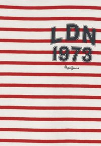 Vitt T-shirt med horisontella röda ränder, med "LDN 1973" i stor svart stil och "Pepe Jeans" skrivet nedanför i kursiv.