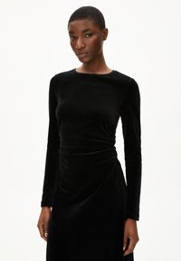 Schwarzes Samt-Kleid mit langen Ärmeln, Rundhalsausschnitt und gerafftem Detail an der Taille. Weiche Textur und glatte Oberfläche.