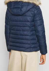 Námořnická prošívaná bunda s kapucí lemovanou kožešinou, s prošívanou texturou a elastickými manžetami. Design je přiléhavý s horizontálními šicími liniemi.