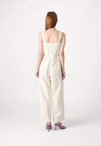 Krämlik overall med en texturerad rygg, vida ben och två bakfickor. Matchad med lila högklackade sandaler.