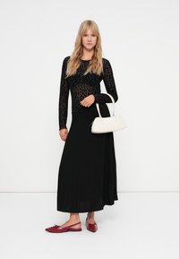 Top negru cu mâneci lungi, cu imprimeu leopard, fustă maxi plisată neagră, pantofi plat roșii și o geantă albă. Design simplu și elegant.