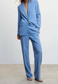Lichtblauwe op maat gemaakte blazer en bijpassende broek, gemaakt van gladde stof. De blazer heeft een enkele knoop en gelapte revers.