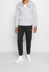 Šedá mikina na zip s tkaničkami, slušivé černé tepláky s malým logem a bílé tenisky. Jednoduchý, neformální sportovní outfit.