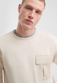 Beige sweatshirt met een ronde hals, uitgerust met een zijzak en ribgebreide kraag. Gladde textuur met een lichte stretch en een minimalistisch ontwerp.