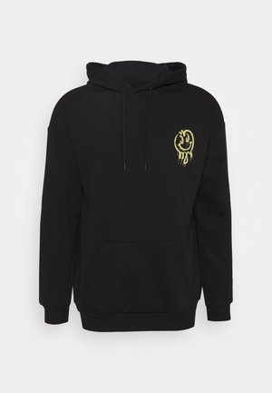 Sudadera negra con bolsillo frontal, capucha con cordones y un gráfico de cara sonriente amarilla goteando en el lado izquierdo del pecho. Textura suave, mezcla de algodón.